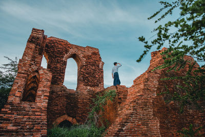 Low angle view of man standing on old ruins against sky