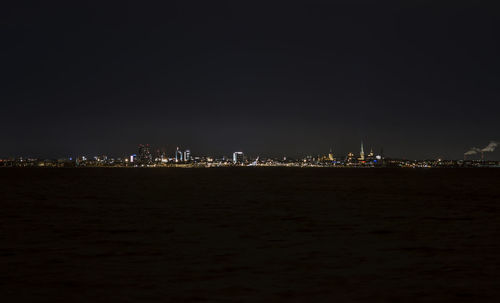 Illuminated cityscape by sea against sky at night