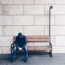 Man sitting on bench against wall