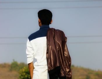 Rear view of man with jacket standing against clear sky
