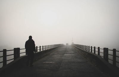 Rear view of silhouette man on railing against sky