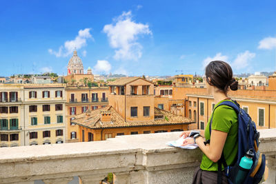 Woman with map looking at building while standing on terrace in city