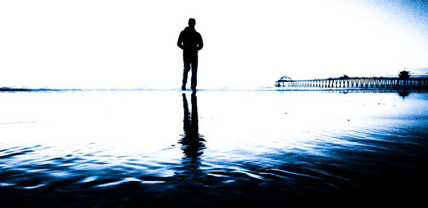 Rear view of silhouette man standing by sea against clear sky