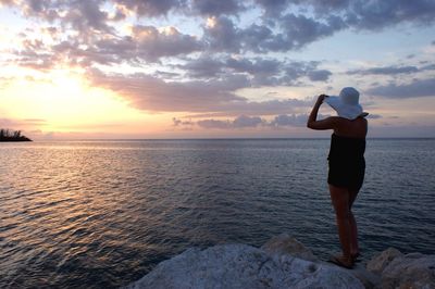 Woman standing in sea against sky during sunset