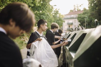 Boys putting plastic garbage in recycling bin