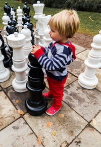 High angle view of cute boy standing amidst chess pieces on board