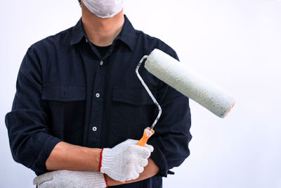 Midsection of worker holding paint roller against white background