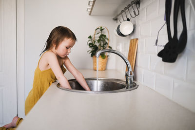 European child of 4 years with water for drink with glass in sink on bright kitchen in real interior