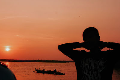 Silhouette people in sea against sky during sunset