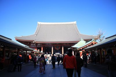 People walking in front of building against clear blue sky