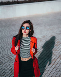 Portrait of beautiful young woman in sunglasses standing on footpath