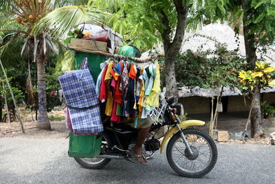 Person carrying stack of clothes while riding motorcycle on street against trees