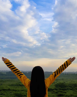 Rear view of woman standing on yellow umbrella against sky