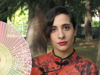 Close-up portrait of young woman holding hand fan in park