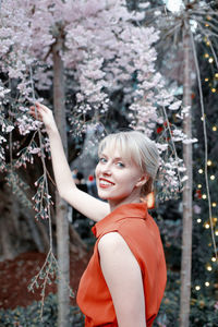 Portrait of beautiful young woman standing by tree