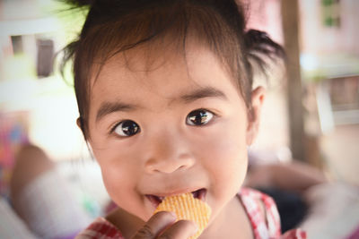 Close-up portrait of cute baby girl eating potato chips