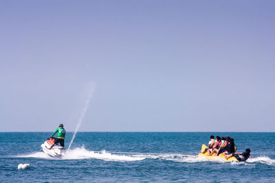 Rear view of man on jet boat pulling people on banana ride in sea