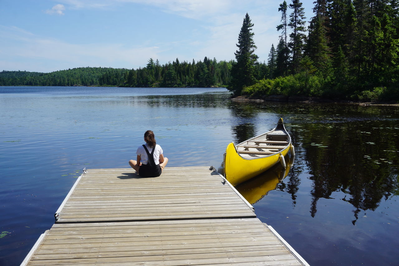 Rear view of teenage girl sitting by lake on jetty