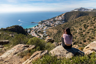 Rear view of woman sitting on cliff against sea