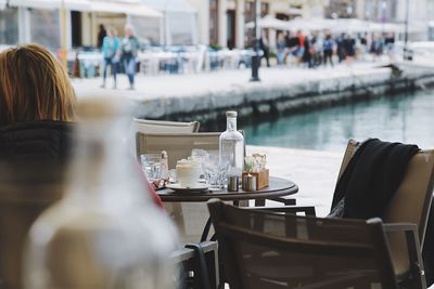 Rear view of woman sitting in outdoors restaurant by water 