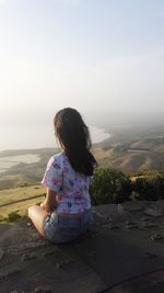 Rear view of woman sitting on landscape against sky