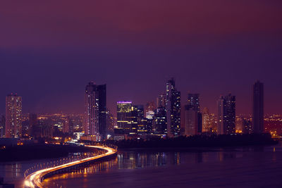 Illuminated buildings by river against sky at night