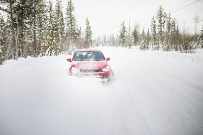 Front view of red car driving on snow covered road.