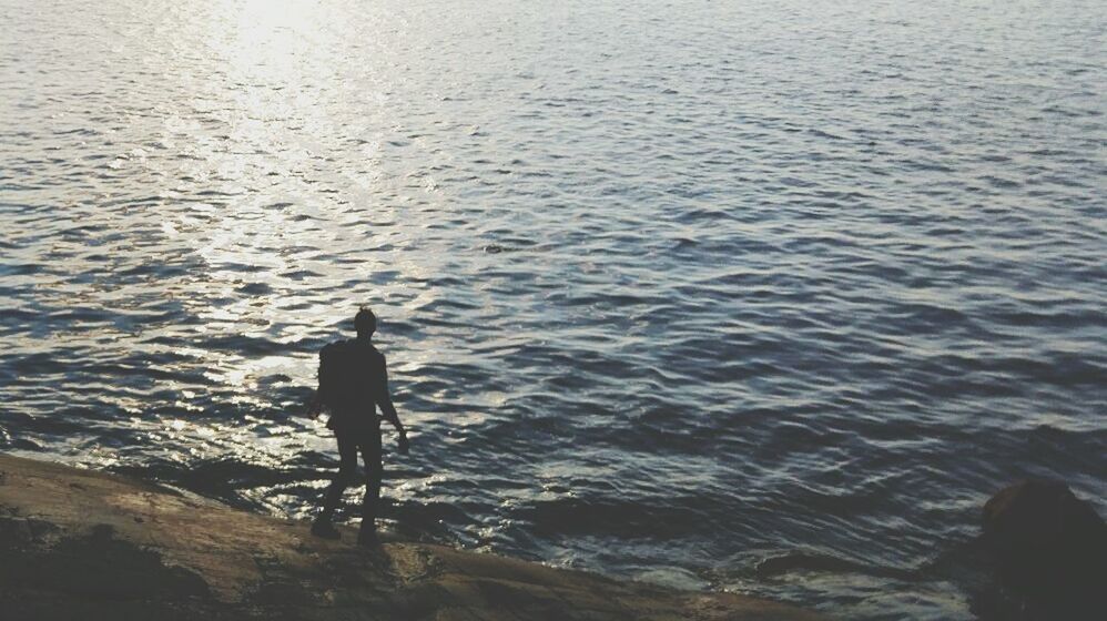 MAN STANDING IN WATER AT SHORE