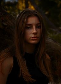 Portrait of young woman with brown hair by tree trunk
