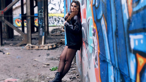 Portrait of young woman leaning on graffiti wall