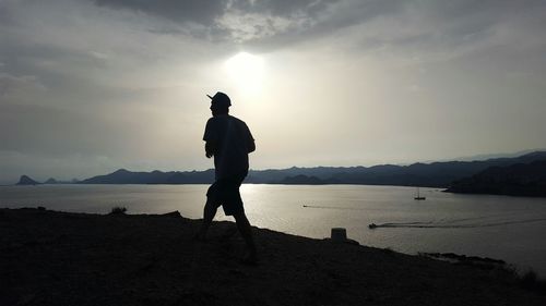Silhouette man standing on shore against sky during sunset