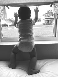 Rear view of boy looking through window at home