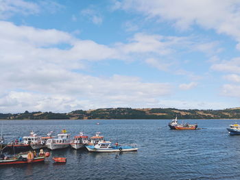 Boats moored in sea against cloudy sky