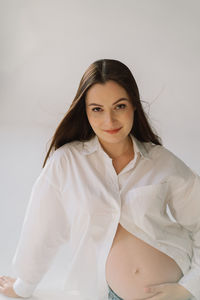 Cute young pregnant girl sitting on the white studio in warm light