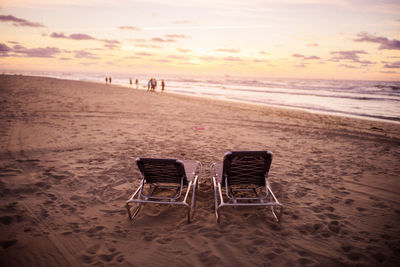 Empty chairs at beach during sunset