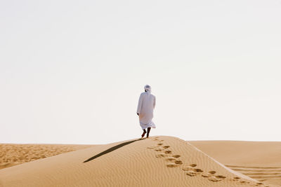 Rear view of man walking at desert against clear sky