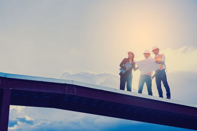 Low angle view of people standing on bridge against sky