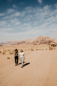 People on sand dune in desert against sky