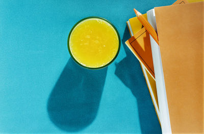 Fresh orange juice in blue glass on blue background , books with orange covers and  orange pencil ,