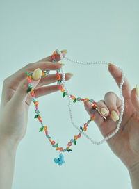 Cropped hand of woman holding bracelet against white background