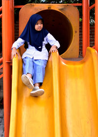 Full length of girl sitting on slide at playground