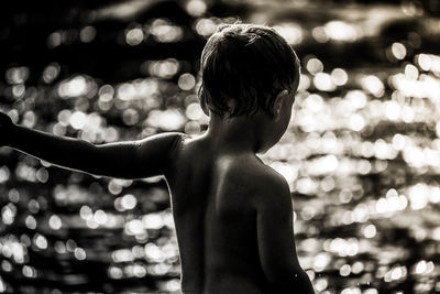 Rear view of shirtless boy in water at night