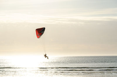Man paragliding over sea against sky during sunset