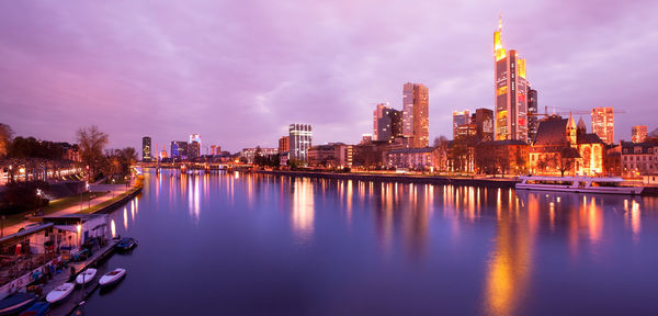 Illuminated buildings by river against sky