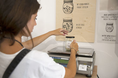 Young woman in packaging-free supermarket weighing goods on scale