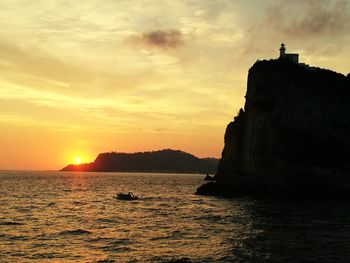 Silhouette rock formation in sea against sky during sunset