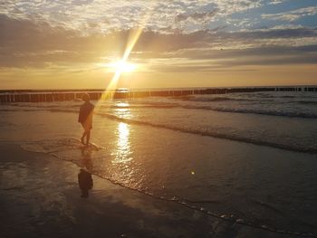 Silhouette boy walking on shore at beach against sky during sunset