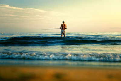 Rear view of shirtless man fishing at sea against sky