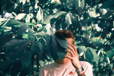 Young man hiding behind plants