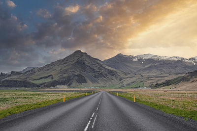 Diminishing road leading towards mountain amidst grass during sunset